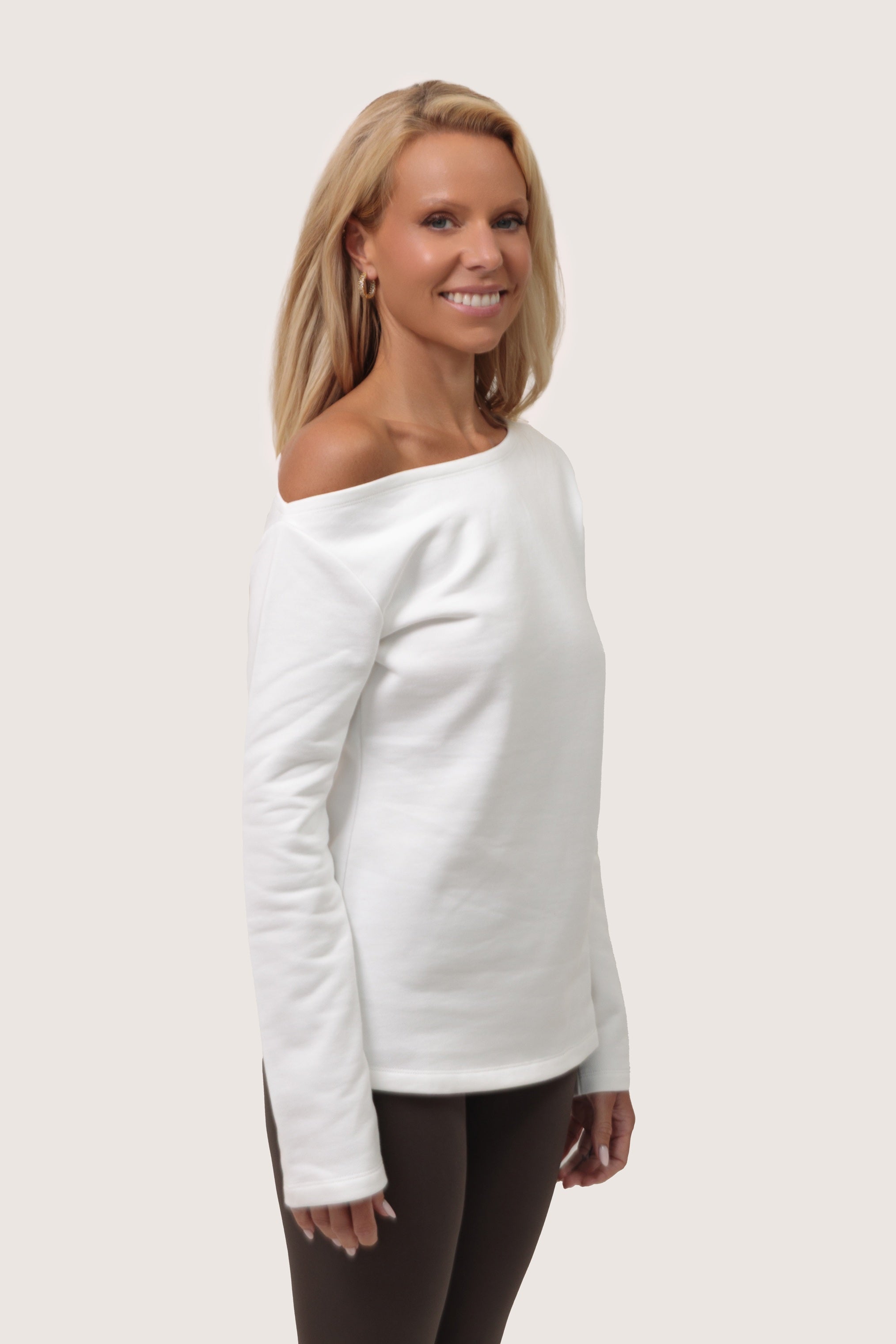 Woman wearing a white off-shoulder sweater on a plain background sidewawys