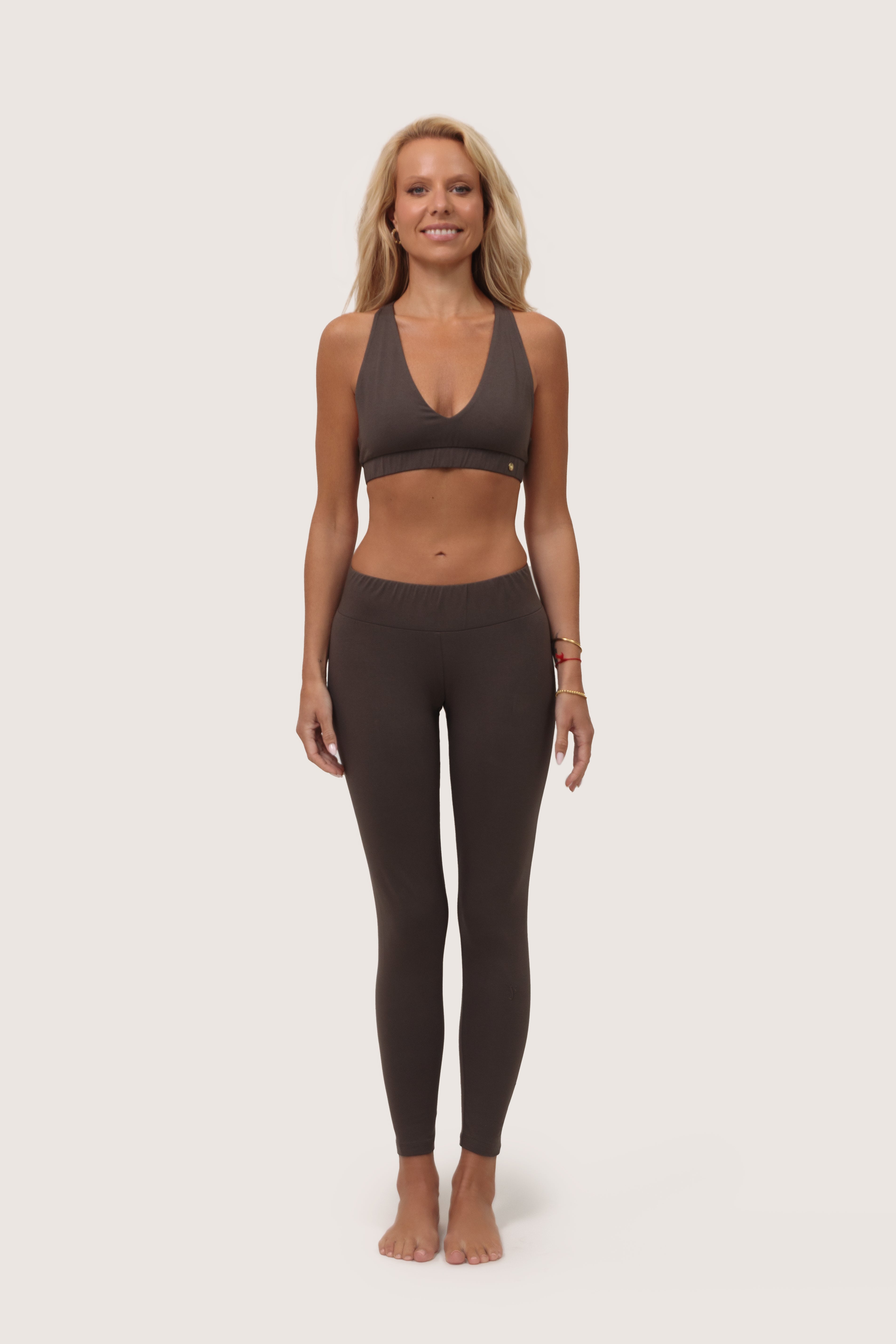 Woman wearing a brown sports bra and leggings made from organic cotton set on a white background