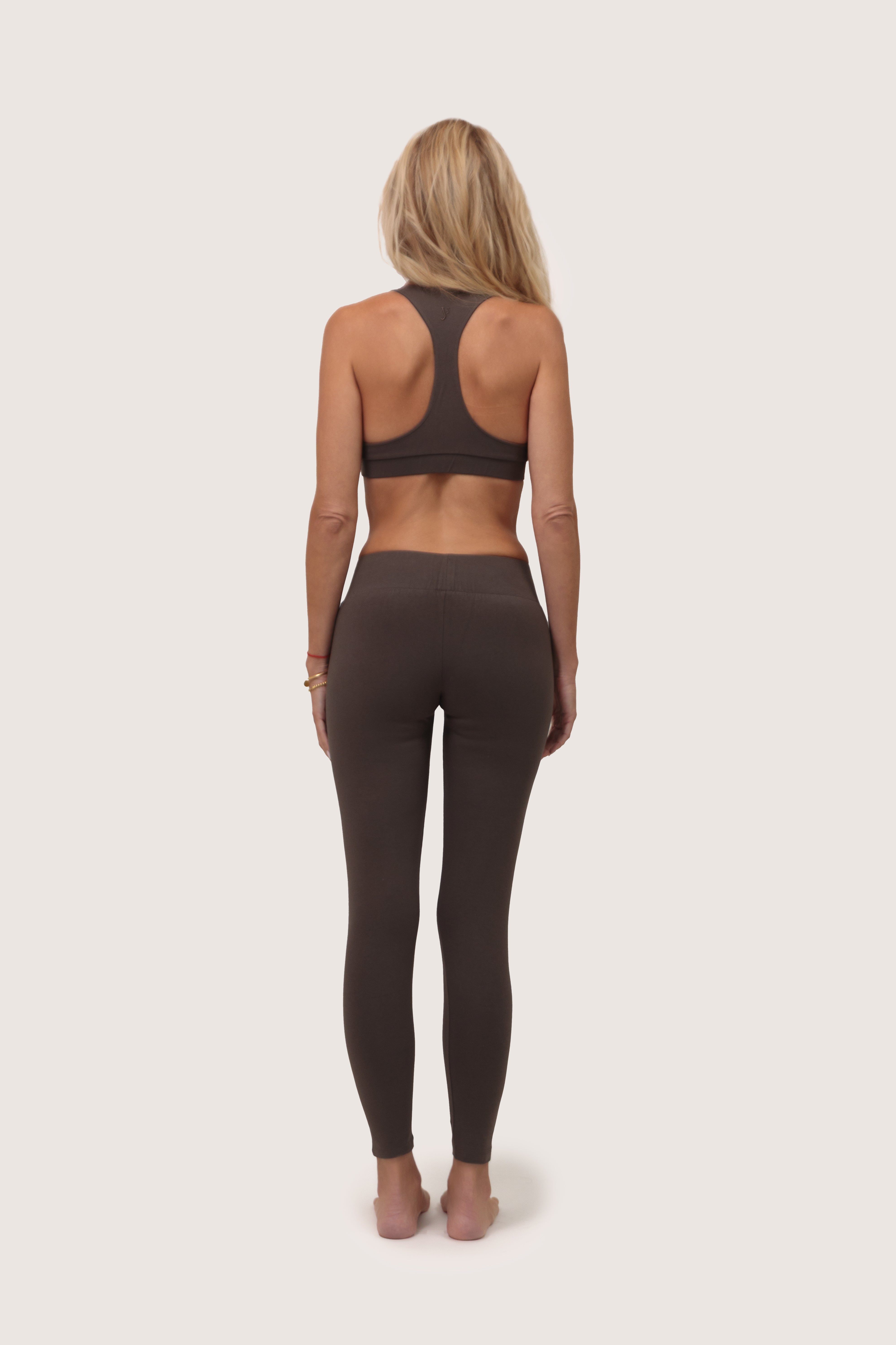 Woman wearing a brown racerback sports bra and matching leggings set on a white background