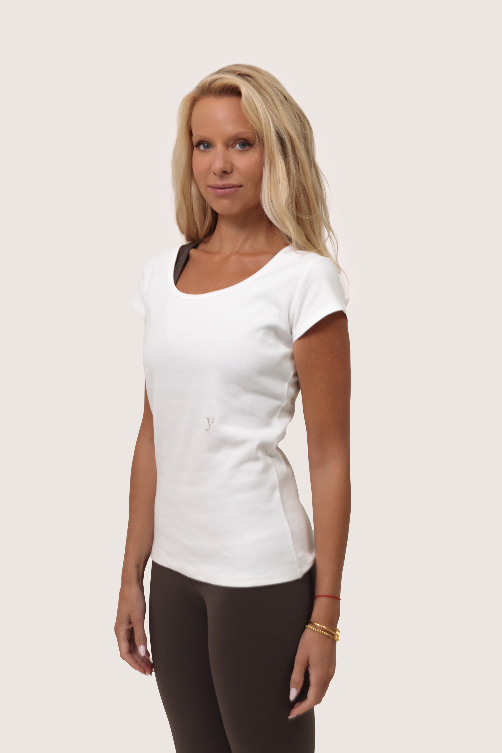 Woman wearing a white tshirt and dark brown pants on a plain background