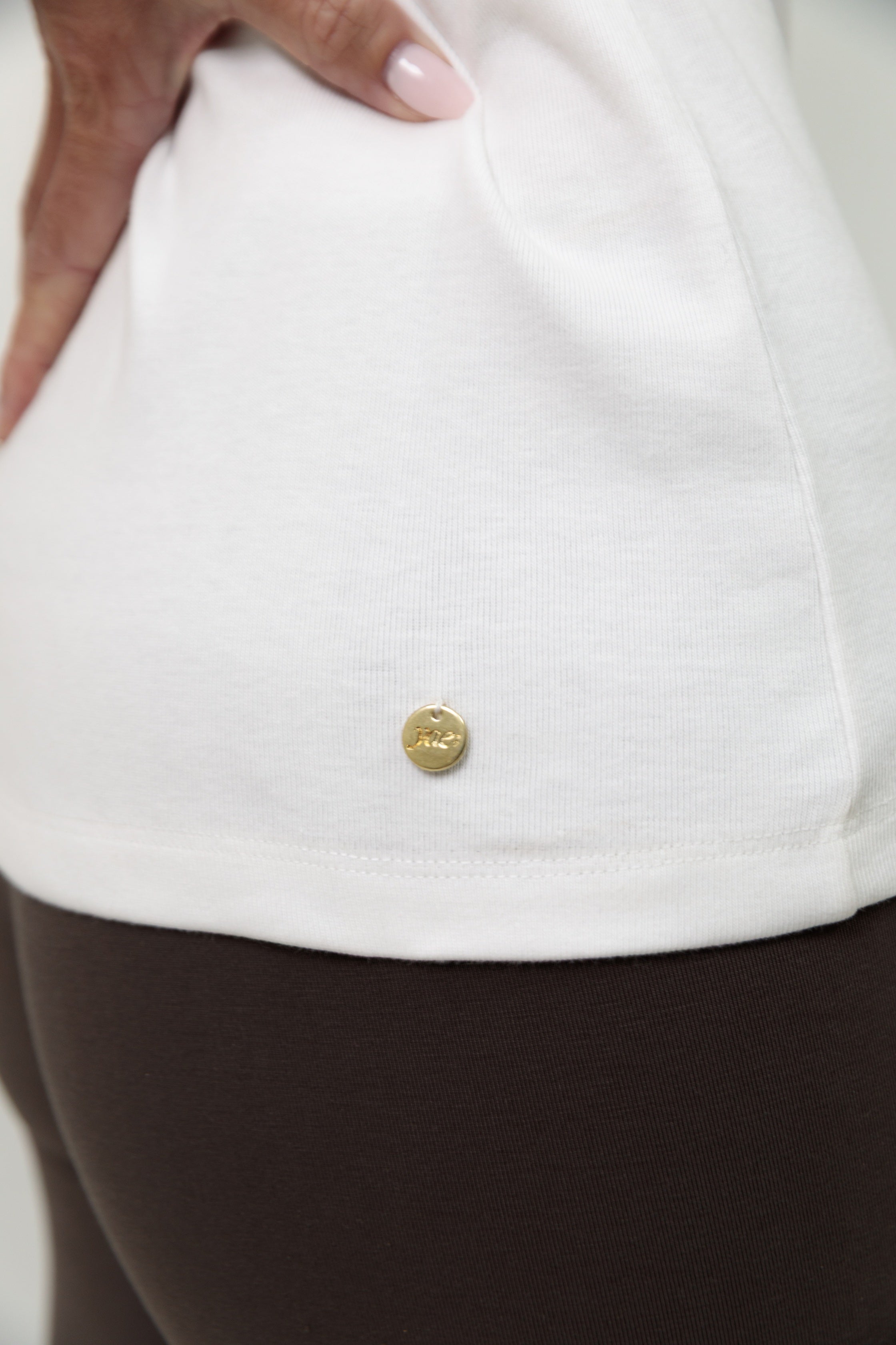 Close-up of a white shirt with a gold branded button on a plain background