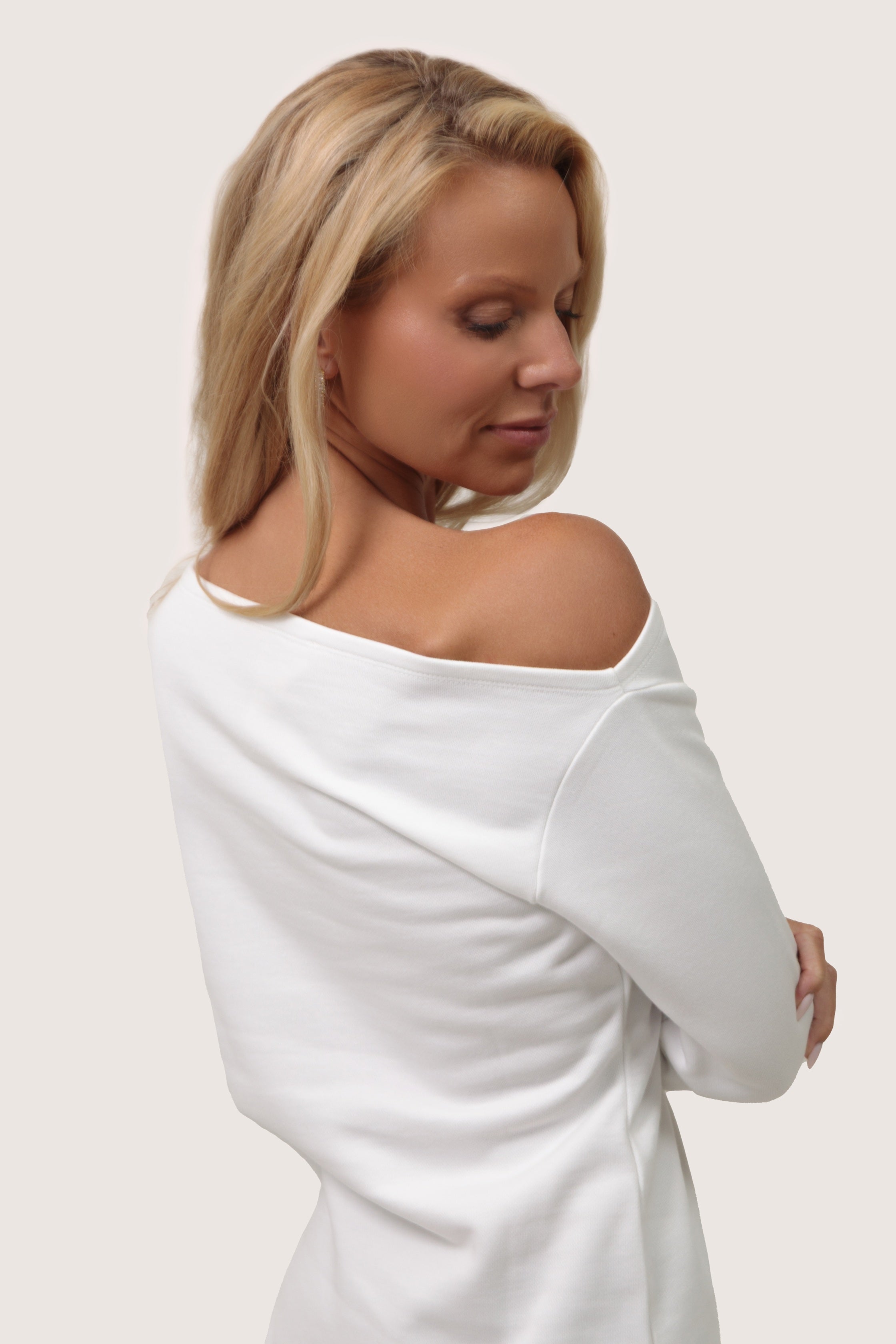 Woman wearing a white off-shoulder top against a plain background